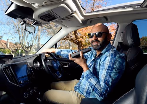 A man wearing sunglasses and a blue plaid shirt is sitting in a car.