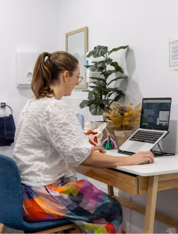 A woman sitting at a desk with a laptop and a potted plant.