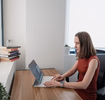 A woman in a red dress is typing on a laptop.